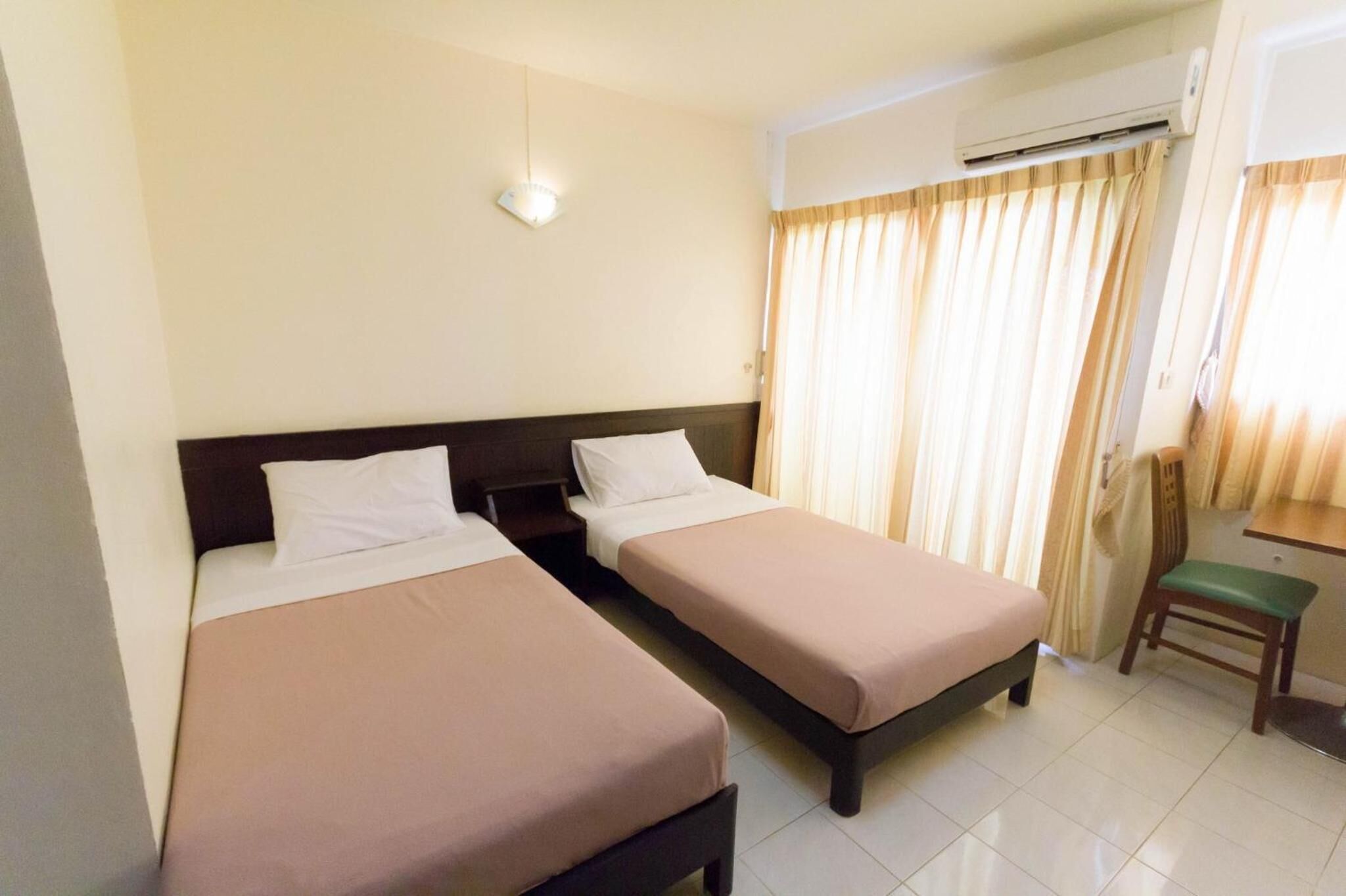 Quarto de hotel com duas camas de solteiro, uma mesa pequena, uma cadeira e um ar condicionado.