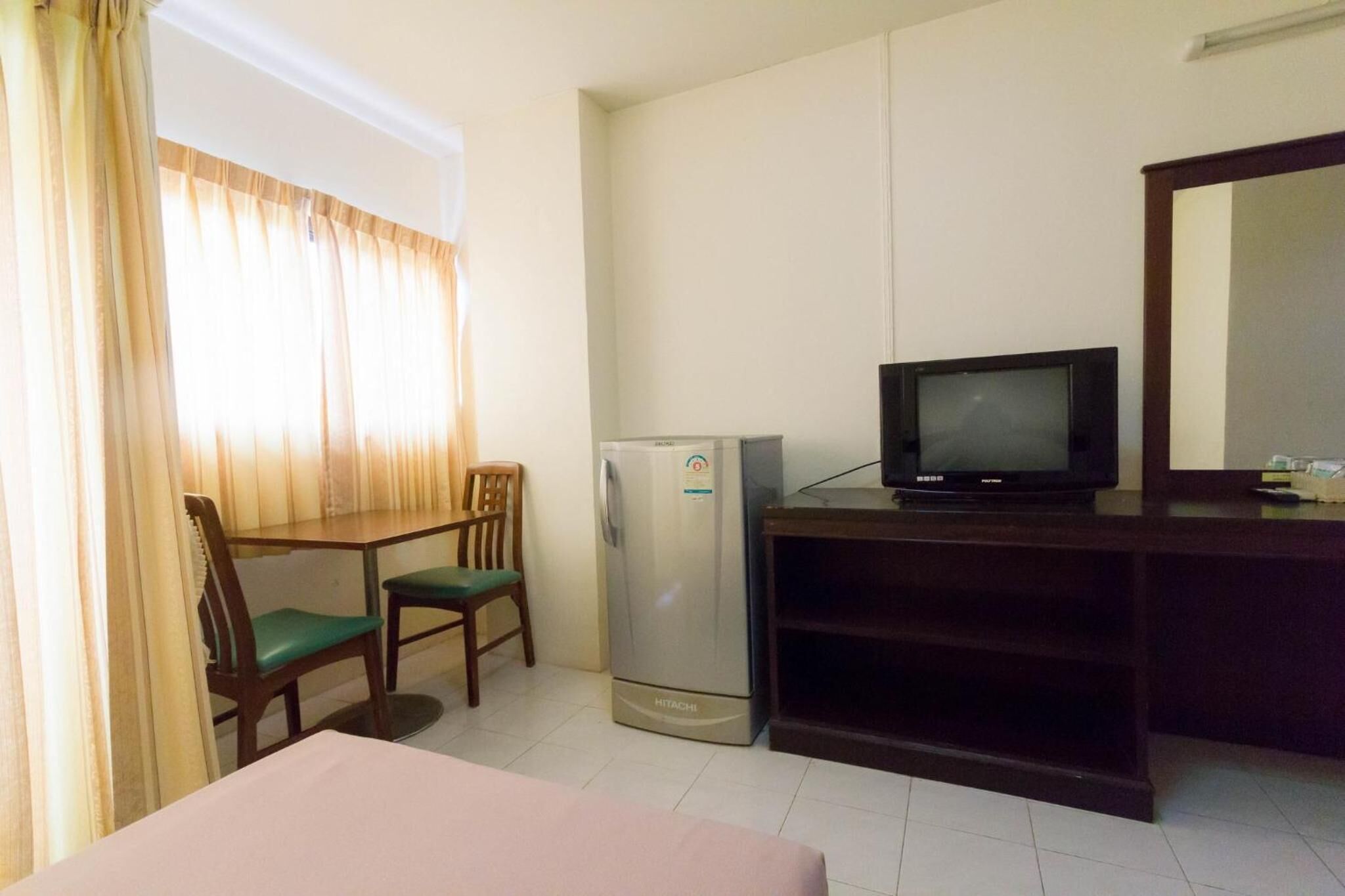 A hotel room with a bed, a desk with a computer, a refrigerator, a television, and a window with curtains.