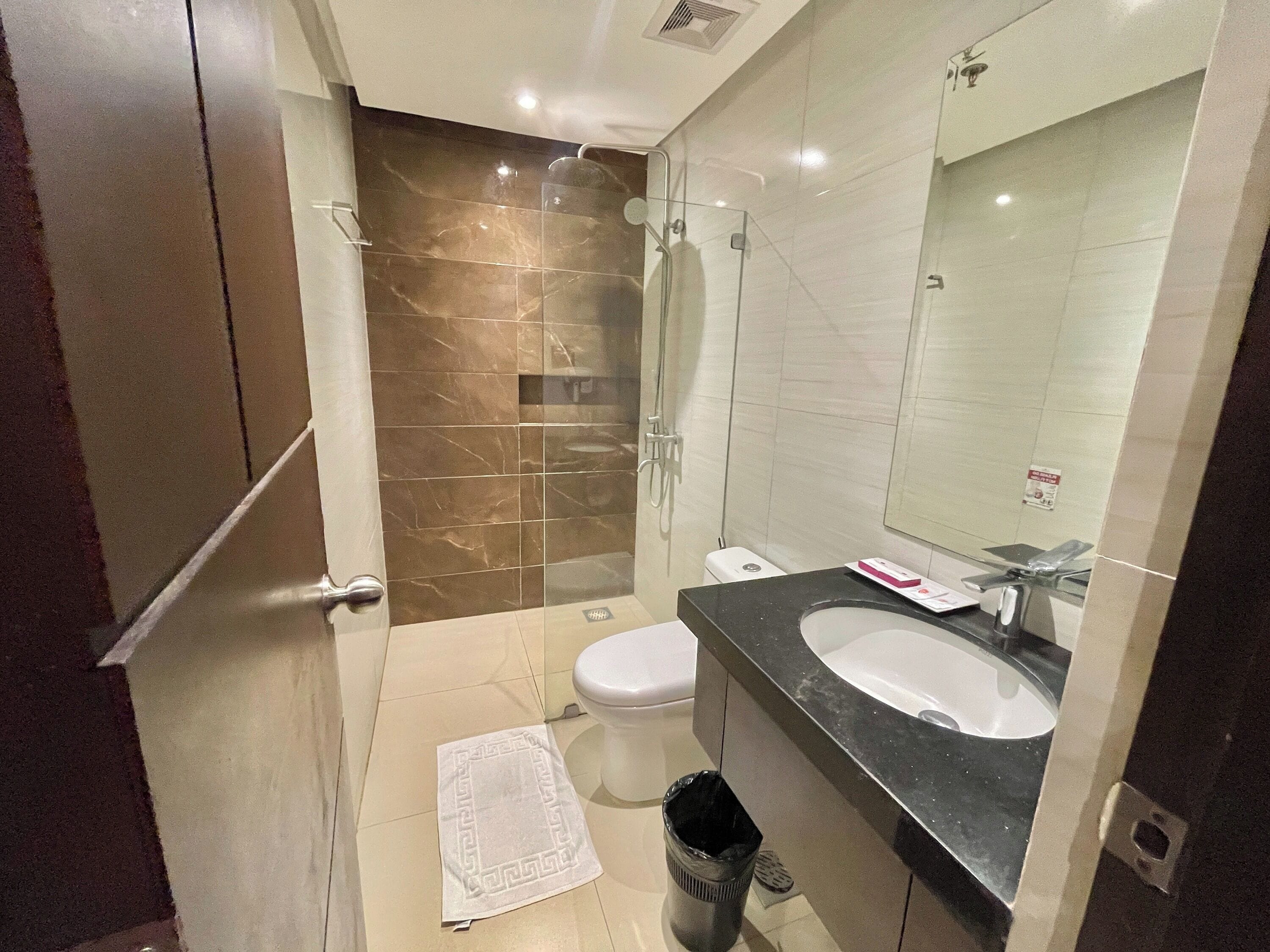 Un baño moderno con cabina de ducha de vidrio, inodoro, lavamanos y espejo.