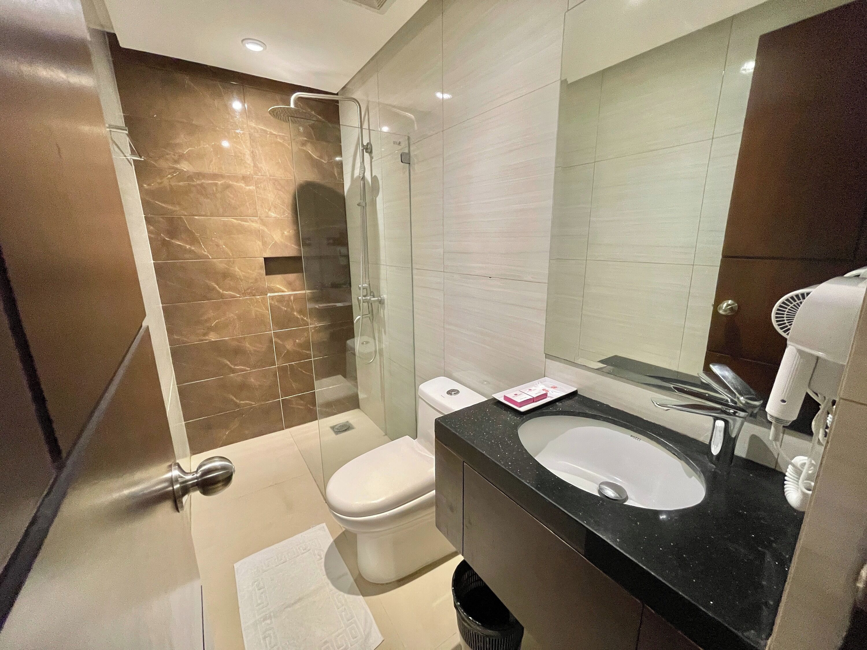 Een moderne badkamer met een douchecabine van glas, een toilet, een wastafel met spiegel en een haardroger.