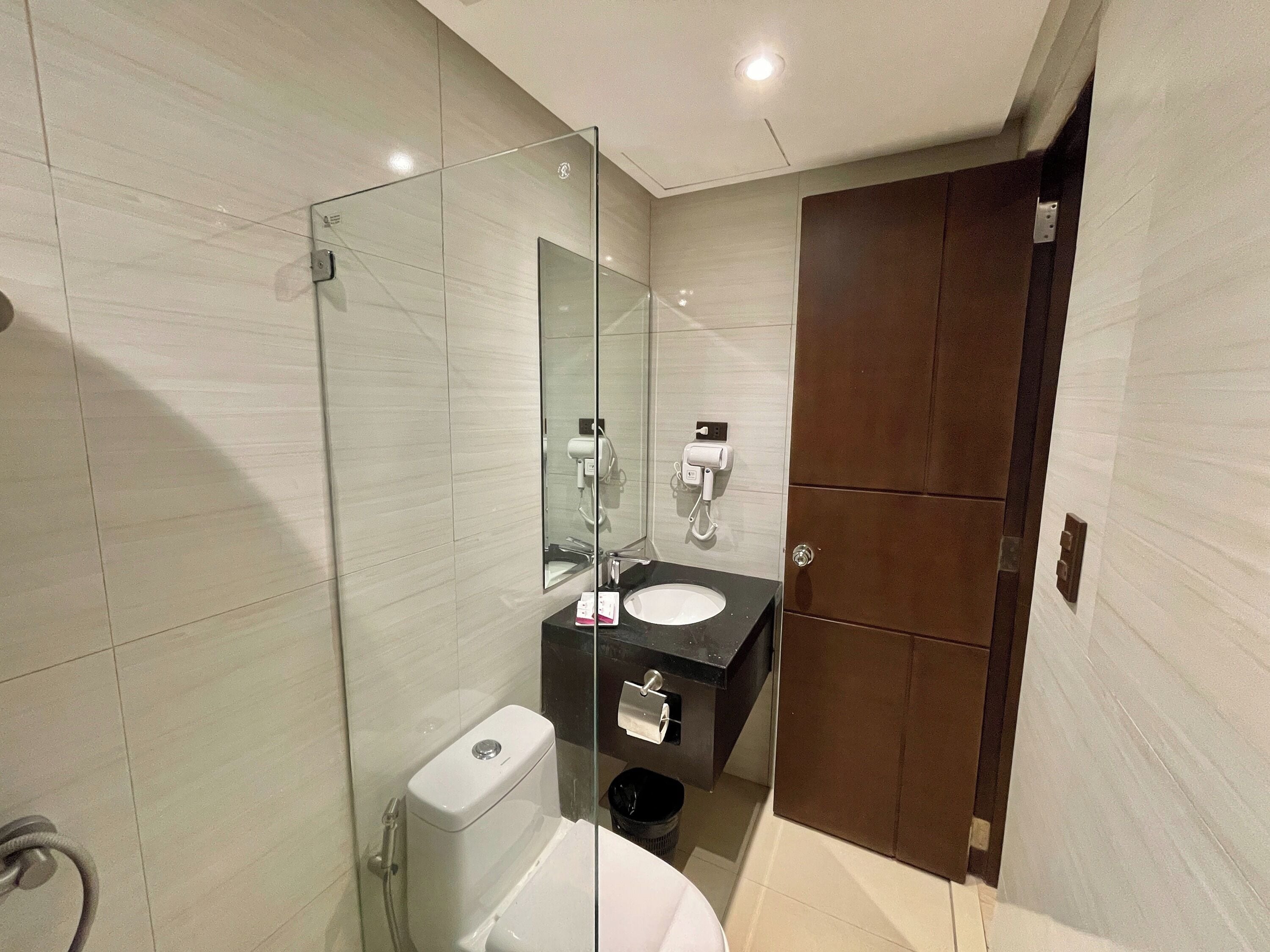Een moderne badkamer met een douchecabine van glas, een toilet, een wastafel en een donker houten deur.