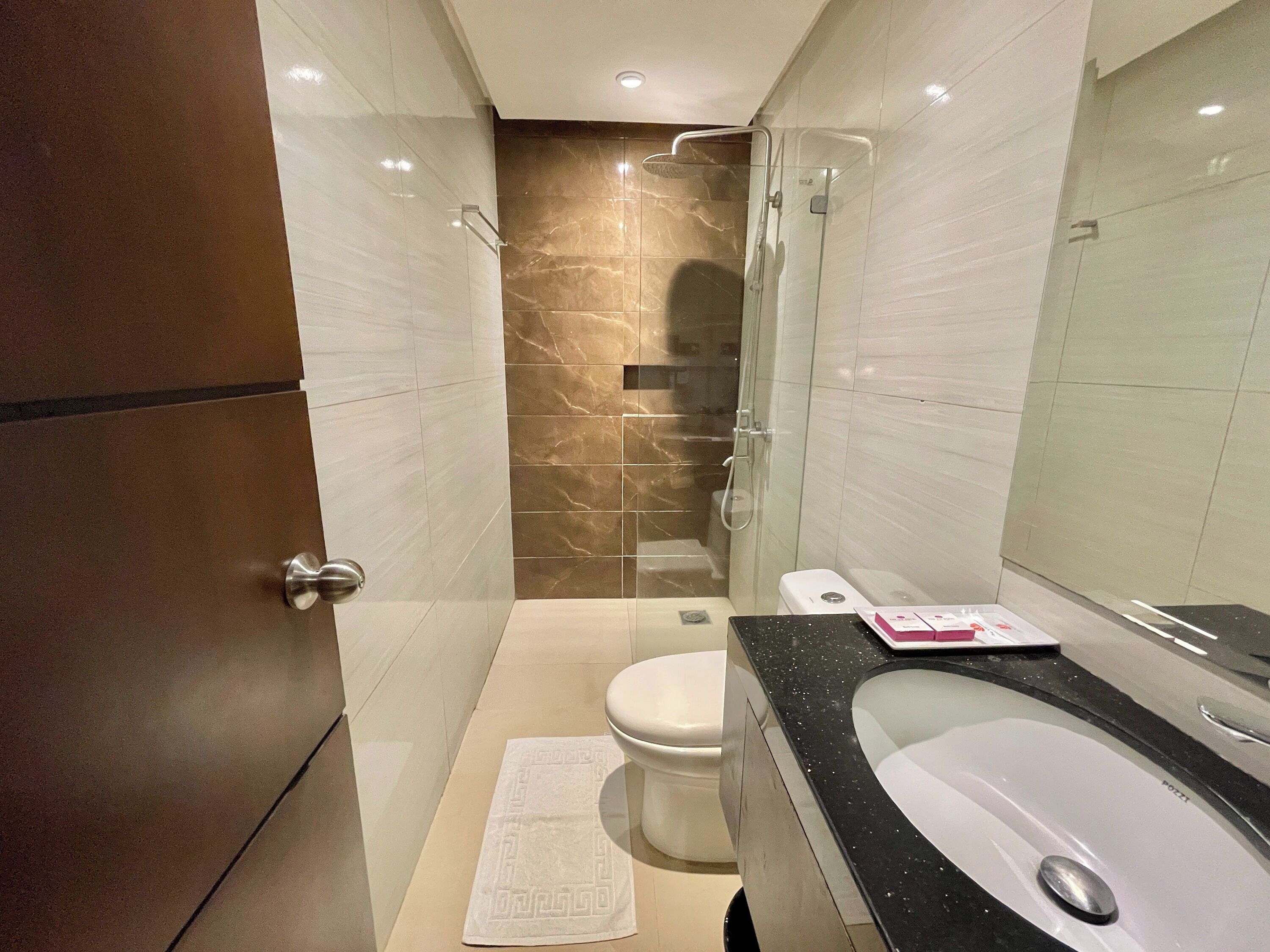 Une salle de bain moderne avec une douche à l’italienne en verre, des toilettes blanches et un lavabo sur un plan de travail noir.