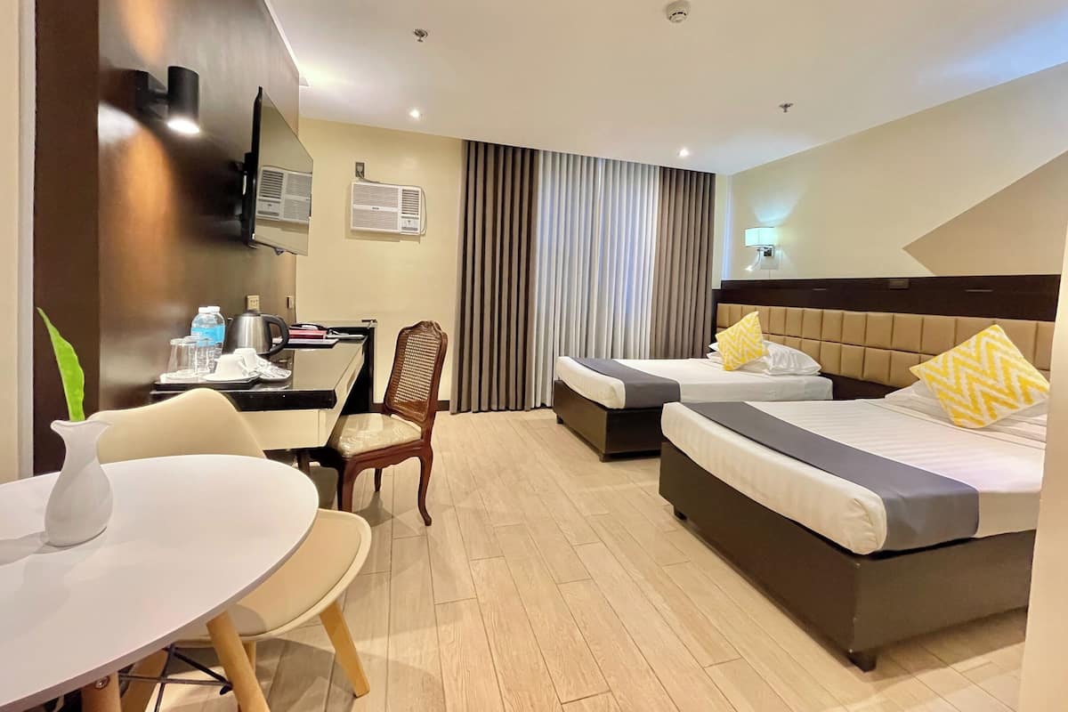 A hotel room with two beds, a desk, a chair, and a small table.
