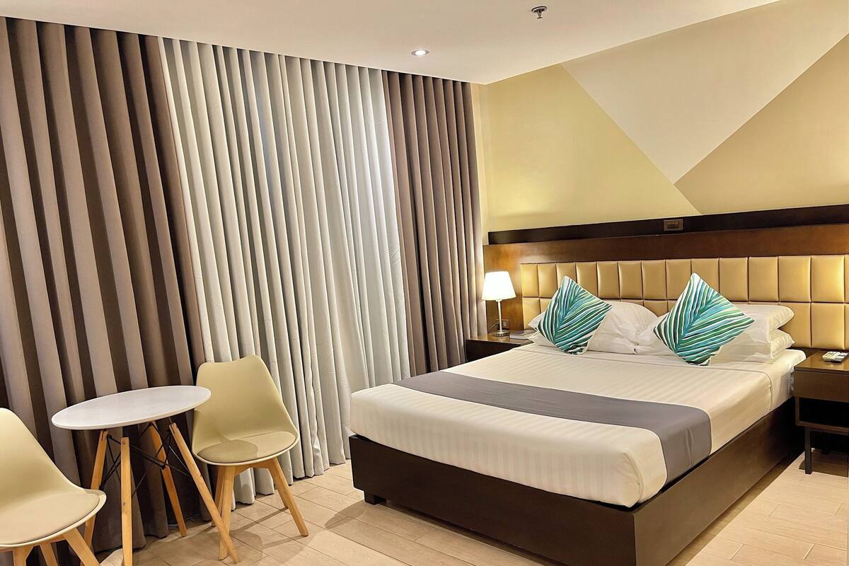A hotel room with a large bed, two chairs, a nightstand, and a lamp.