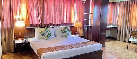 Habitación de hotel con una cama grande, dos lámparas de noche, un equipo de aire acondicionado y suelo de madera.