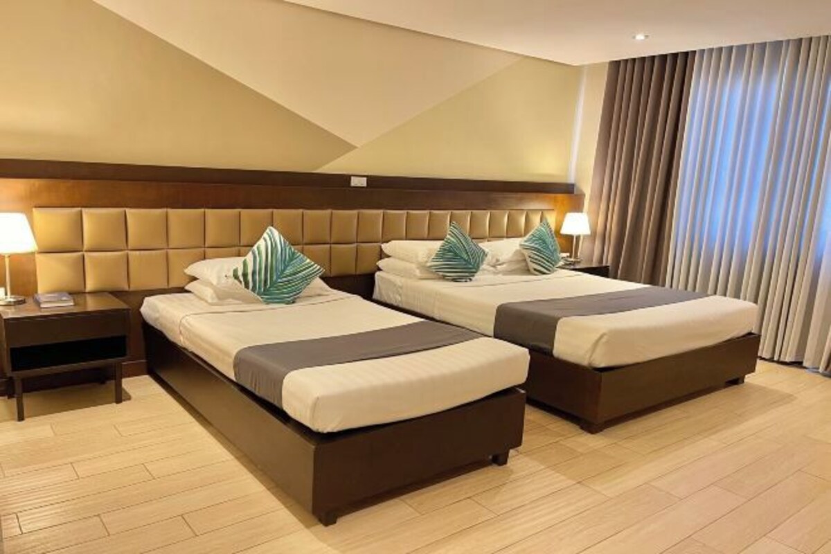 Una habitación de hotel con dos camas, un cabecero de madera, una mesita de noche y una lámpara.