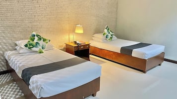 Habitación de hotel con dos camas, una mesita de noche, una lámpara y una pared de ladrillo.