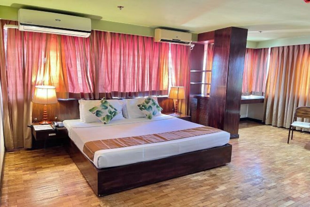 Habitación de hotel con una cama grande, dos lámparas de noche, un equipo de aire acondicionado y piso de madera.