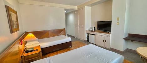A hotel room with two beds, a desk with a TV, and a small kitchenette.