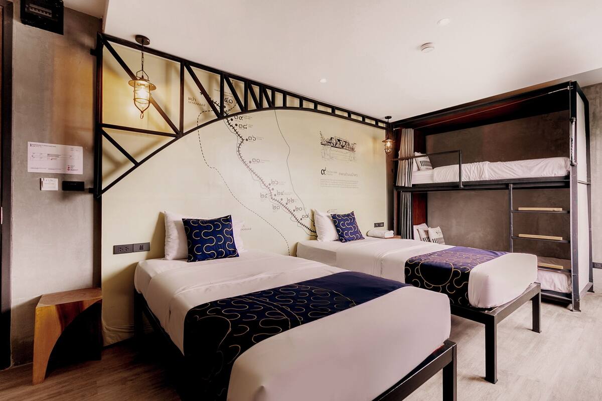 A hotel room with two beds, a bunk bed, a map on the wall, and a wooden bench.