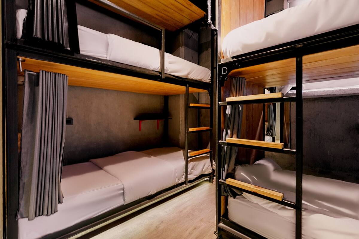 A bunk bed room with wooden bunk beds, a small shelf, and a curtain.