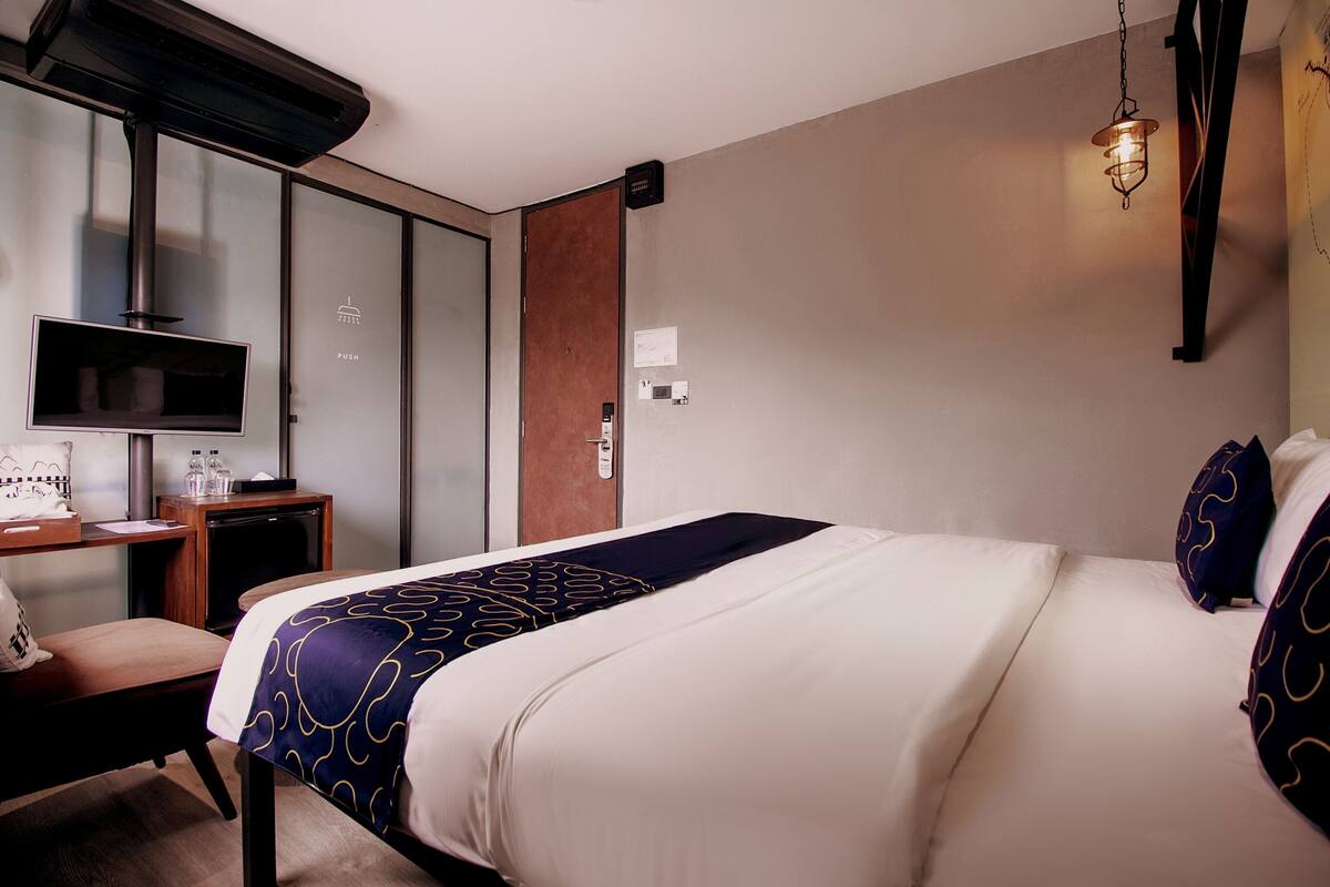 A hotel room with a bed, a desk, a television, and a wall-mounted heater.