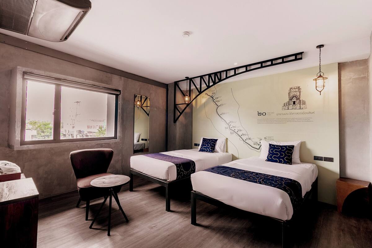 A modern hotel room with two beds, a desk, a chair, and a large window.