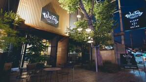Un espacio al aire libre con mesas y sillas, una terraza de madera y un letrero que dice 'Westory Design Posthotel' publicitando servicios de descanso, comida y bebida.
