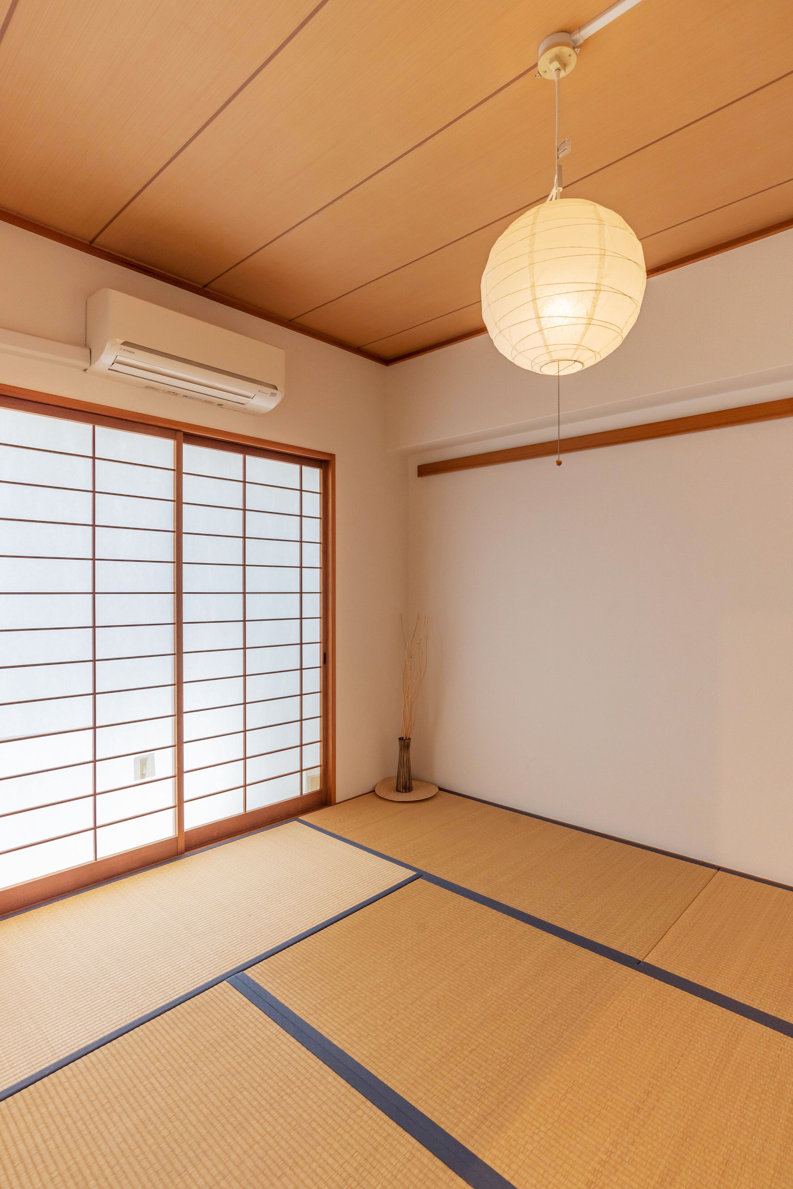 A room with tatami flooring, a sliding shoji screen door, an air conditioning unit, and a hanging paper lantern.