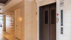 A modern elevator with a control panel, a door with a safety sign, and a corridor with a glass door. - Universal Bay Condominium (Osaka)