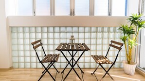 A room with a wooden table and chairs, a potted plant, and a window with blinds. - Universal Bay Condominium (Osaka)