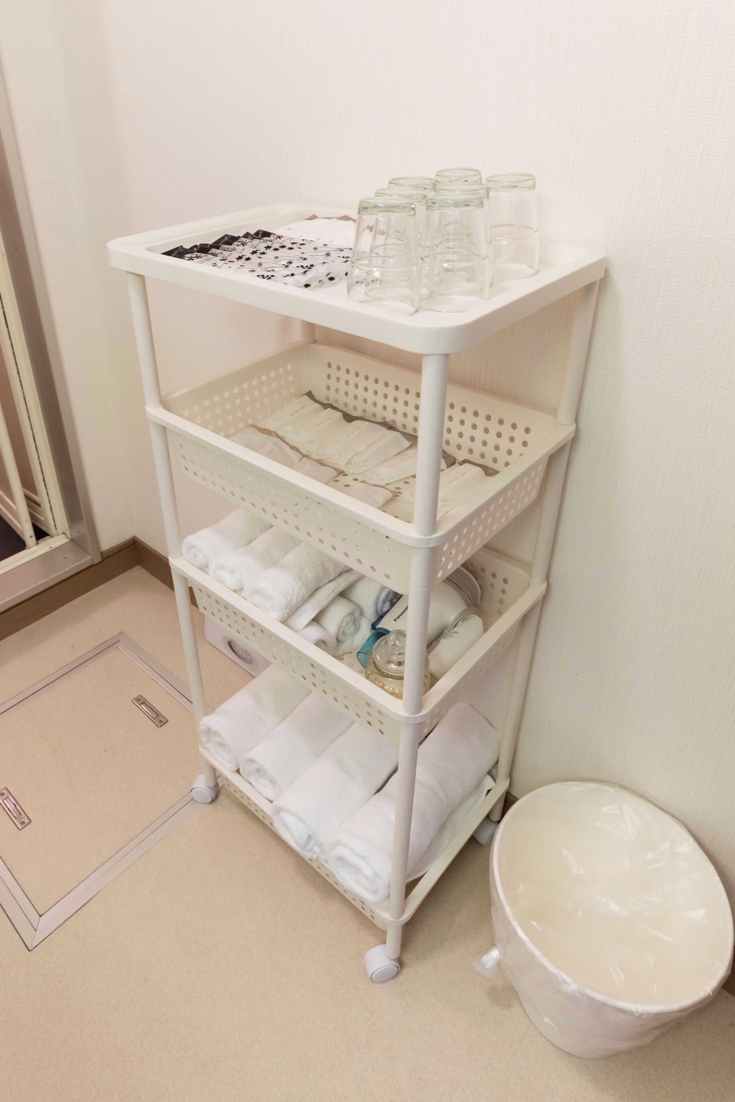 A white metal storage cart with multiple shelves, some containing folded towels and a glass jar.