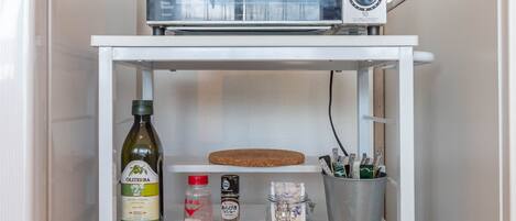 A kitchen with a microwave, a rice cooker, a kettle, and various condiments on a white shelf.