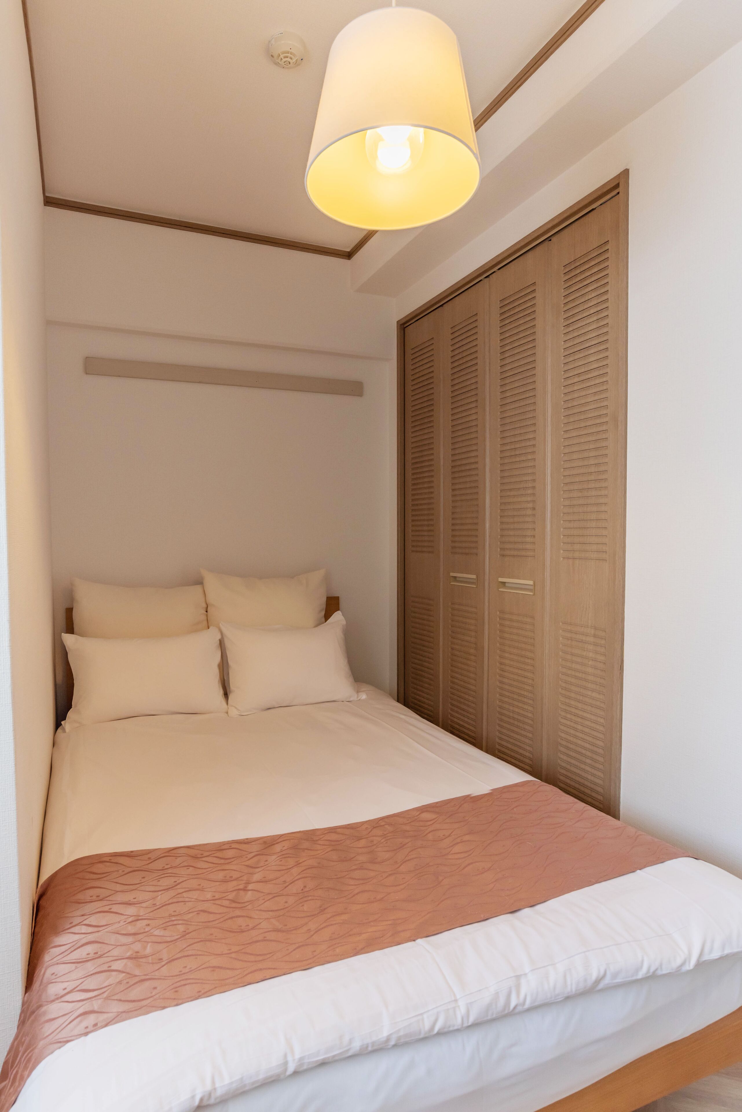A bedroom with a bed, a wooden wardrobe, and a ceiling light fixture.
