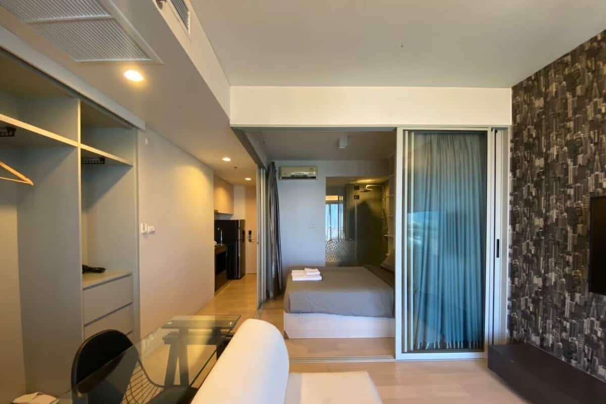 A modern hotel room with a glass dining table, a sofa, a walk-in closet, and a shower area.
