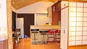 Een keuken met een houten plafond, een koelkast, een spoelbak en drie barstoelen.