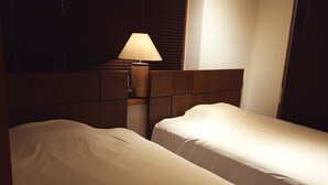 Een hotelkamer met twee enkele bedden, een nachtkastje met een lamp en een hoofdeinde.