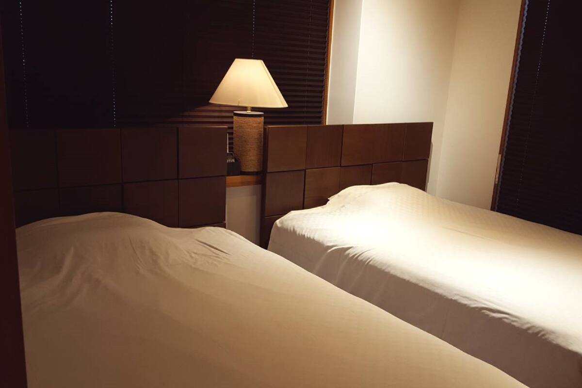 Une chambre d’hôtel avec deux lits simples, une table de chevet avec une lampe et une tête de lit.