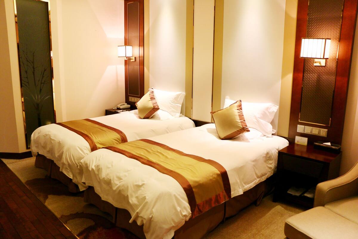 Quarto de hotel com duas camas, uma mesa de cabeceira, uma cadeira e um espelho.