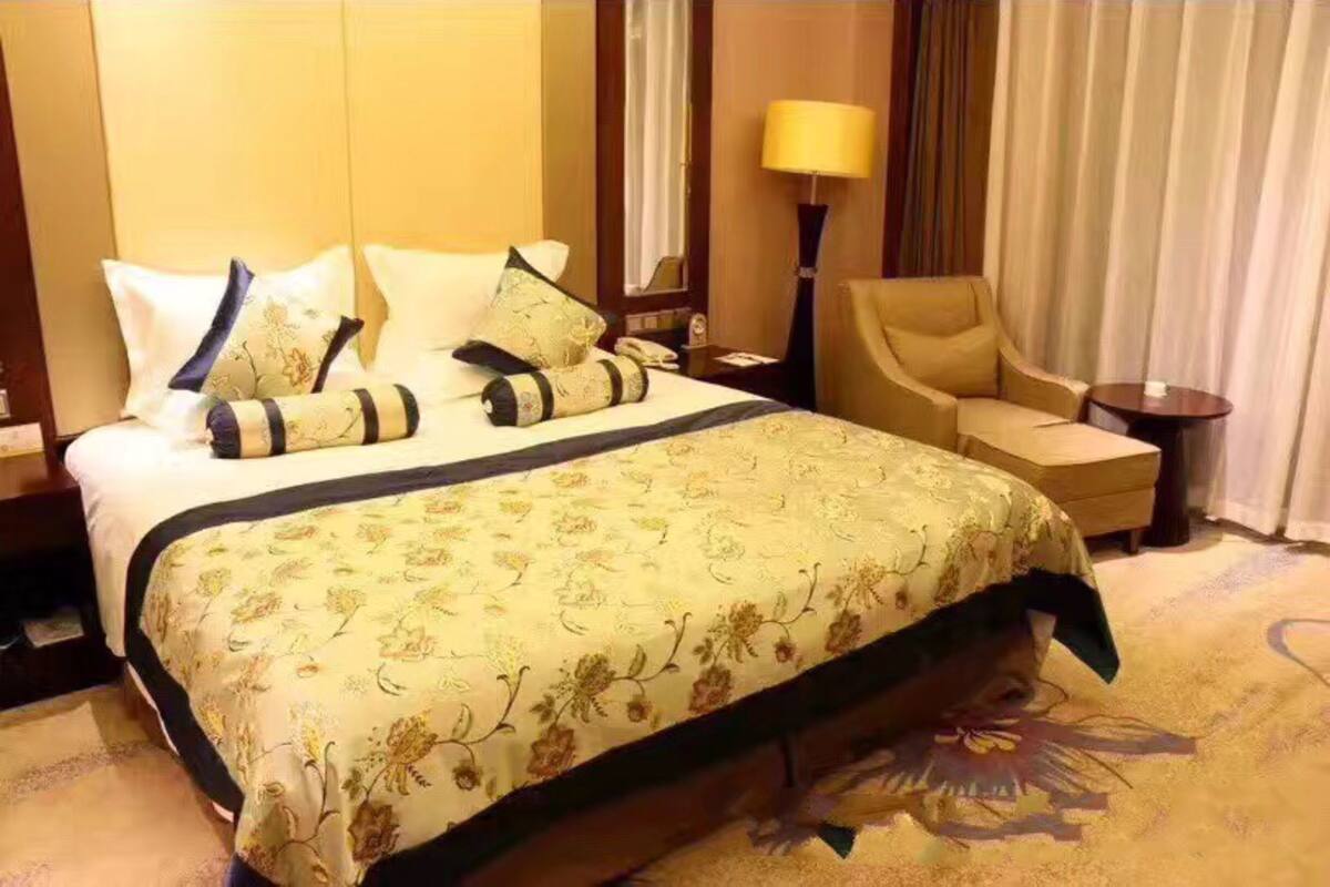 Quarto de hotel com uma cama grande, uma cadeira, uma mesa de cabeceira e uma luminária.