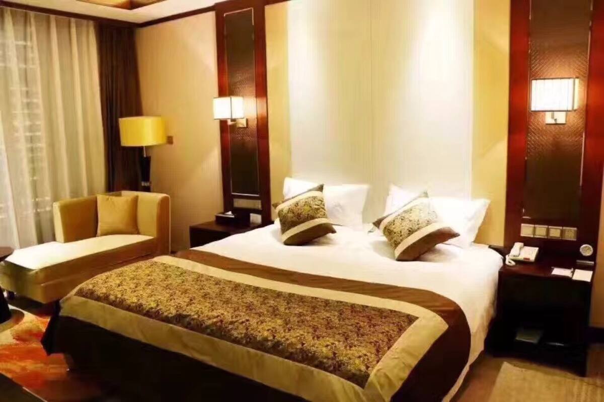 Quarto de hotel com uma cama grande, um sofá, uma escrivaninha com luminária e uma mesa de cabeceira com telefone.