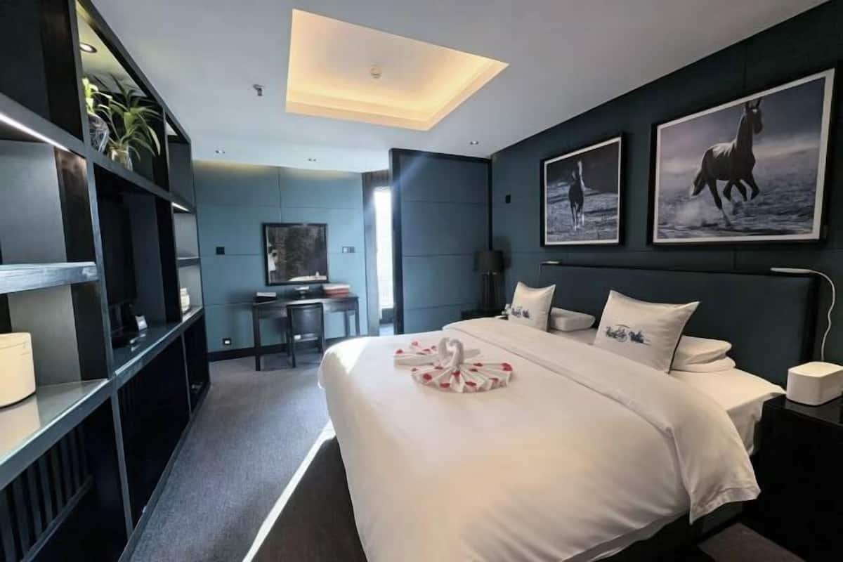 A modern hotel room with a large bed, a desk, and a bookshelf.