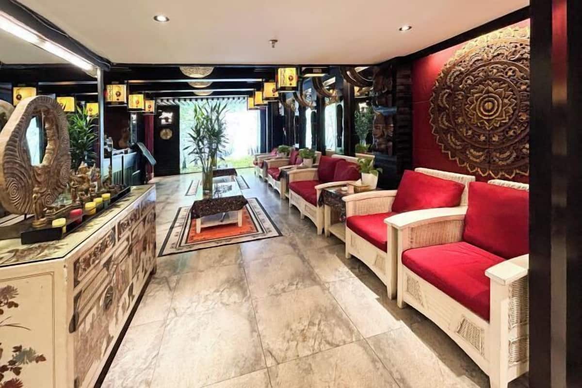 A lobby with a reception desk, seating area with red cushions, decorative wall art, and a large mirror.