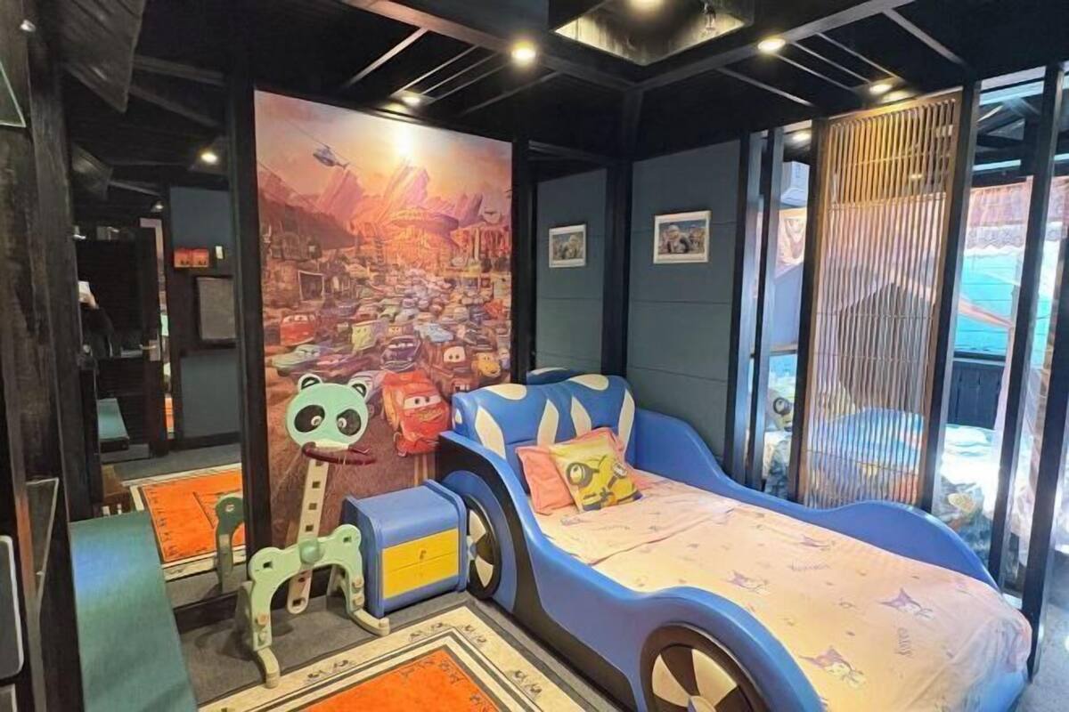 A children's room with a bed shaped like a car, a large mural, and a window with a view.