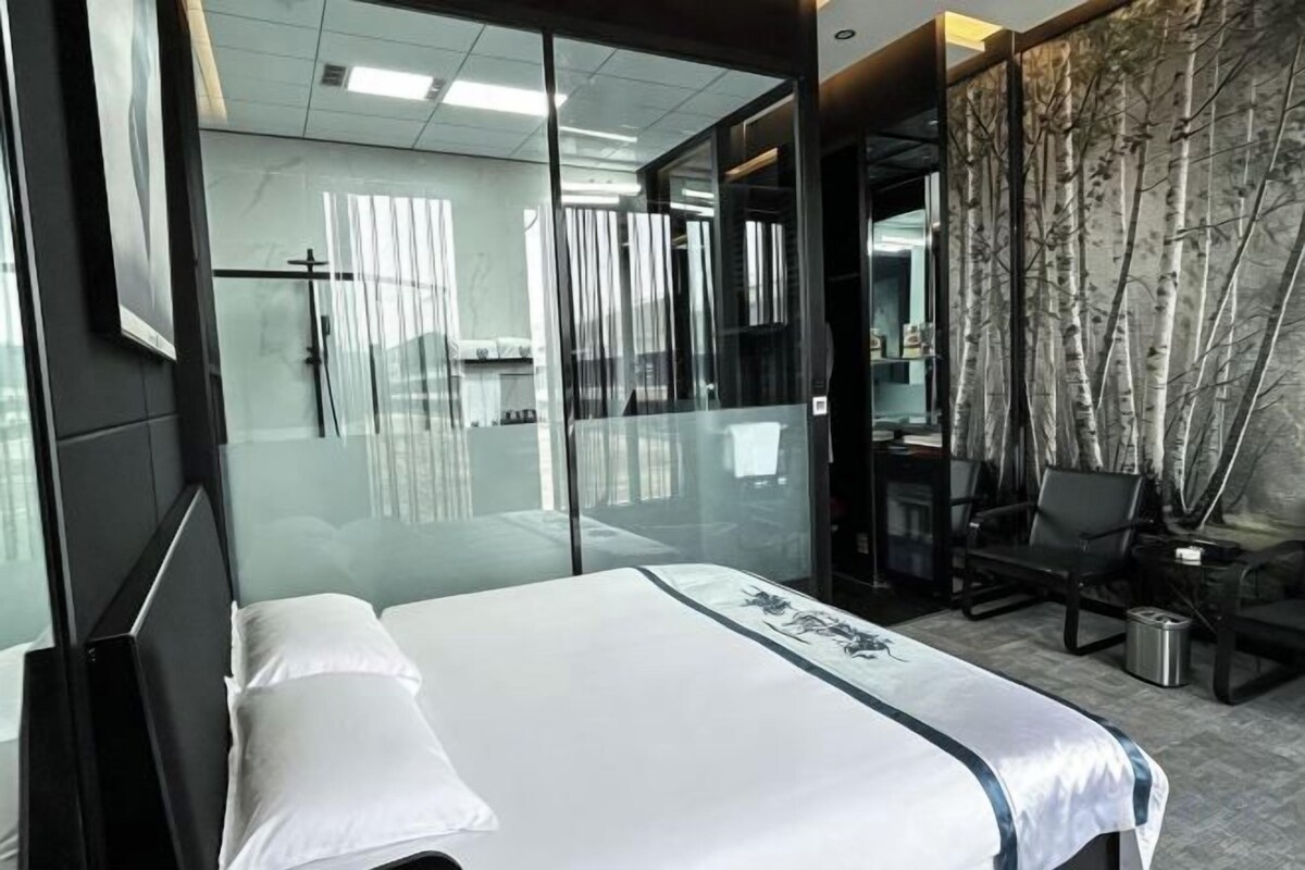 Habitación de hotel con cama, escritorio y silla. Cuenta con un separador de vidrio y vistas al exterior.