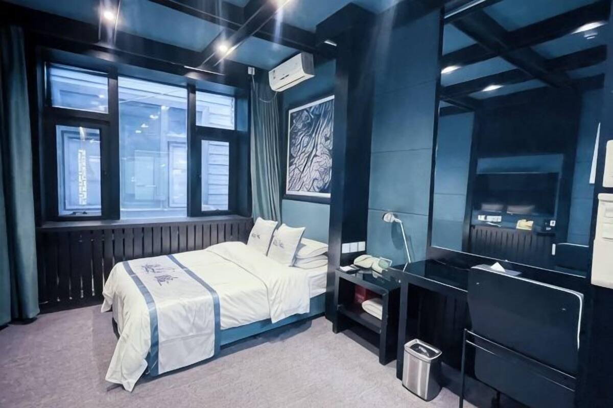 A modern hotel room with a bed, bedside table, lamp, and a large mirror.