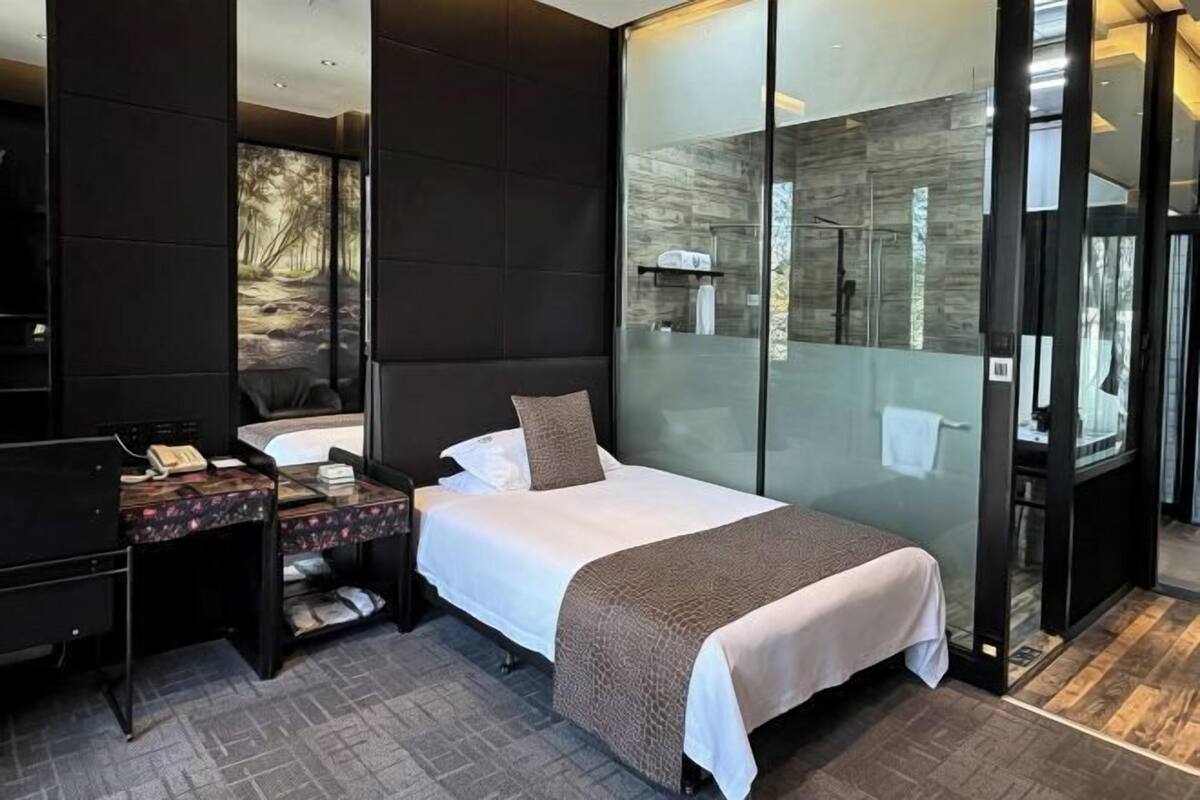 A modern hotel room with a bed, a desk, a phone, and a glass partition.