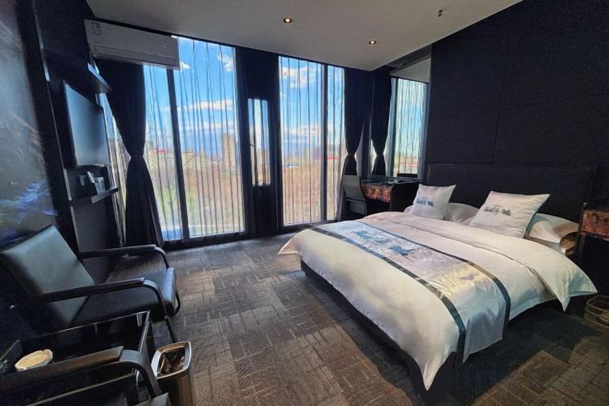 Habitación de hotel con una cama grande, un escritorio, una silla y vistas al exterior a través de amplias ventanas.