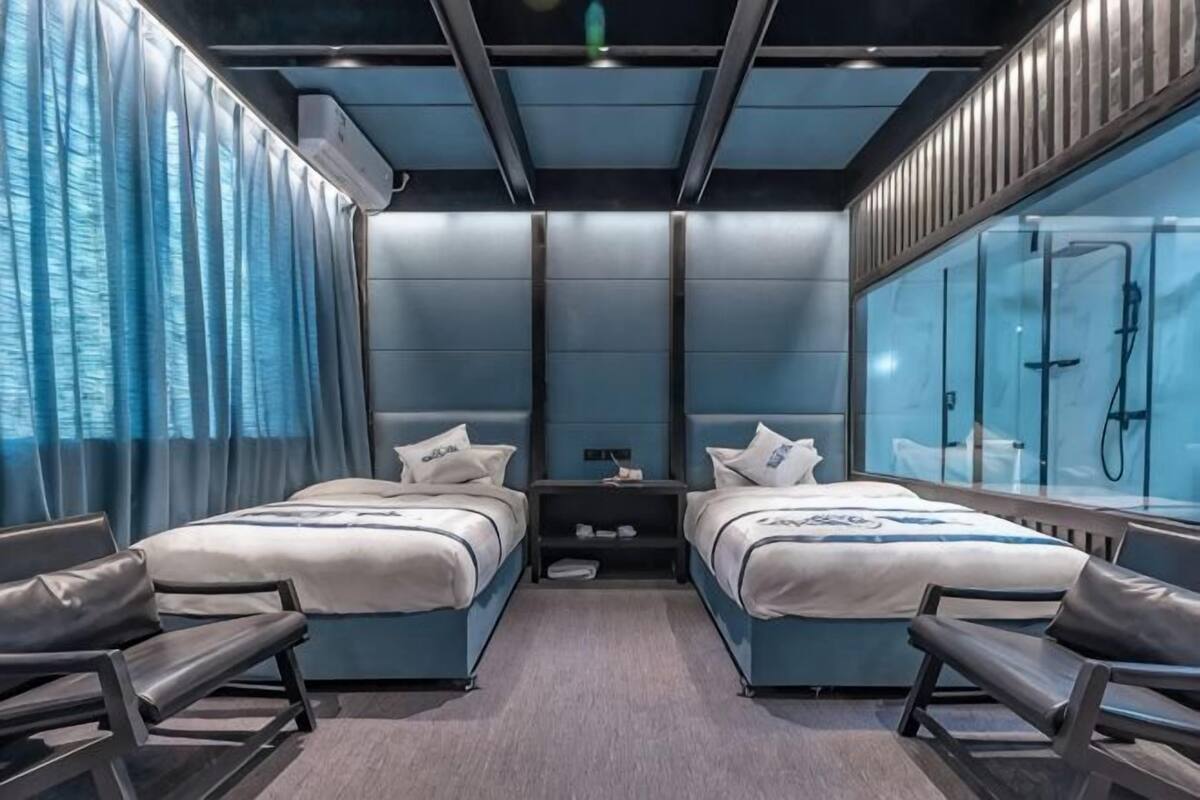 A modern hotel room with two beds, a shower, and a seating area.