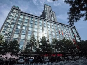 A modern hotel with a glass facade, multiple floors, and a prominent entrance with a red sign.