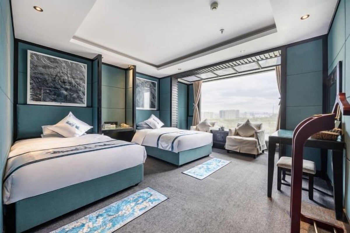 Habitación de hotel con dos camas, un escritorio, una silla y un ventanal con vistas a la ciudad.