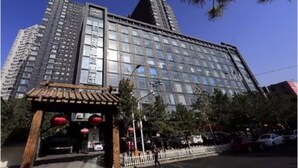 Un edificio moderno de gran altura con varios pisos, grandes ventanales y un área de entrada destacada con una estructura de madera tradicional y faroles rojos.
