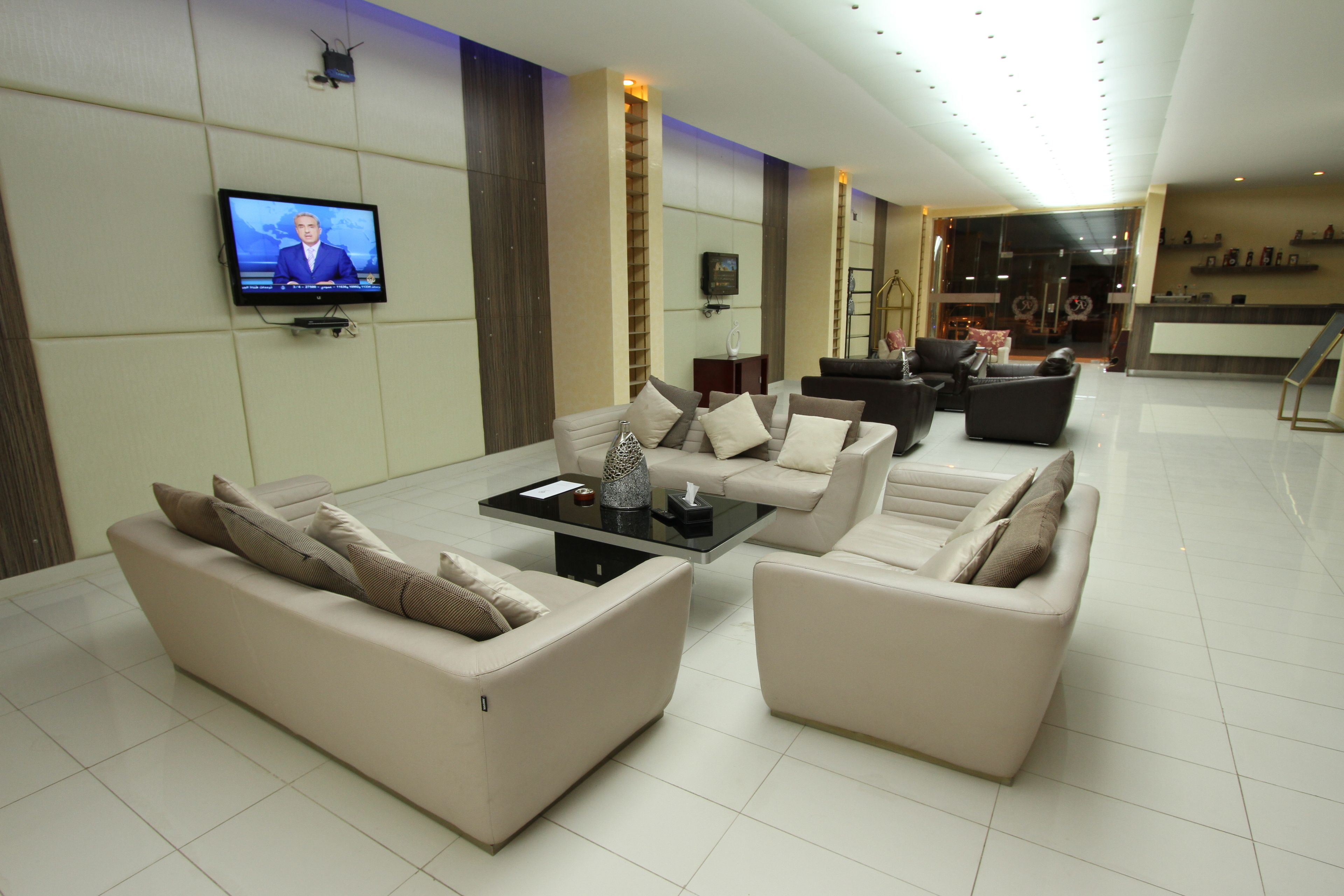 Un moderno vestíbulo de hotel con una televisión de pantalla plana, varios sofás, una mesa de centro y un mostrador de recepción.