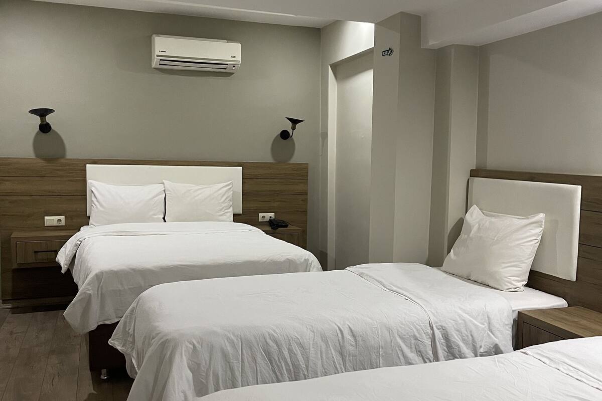 A hotel room with two beds, a wooden headboard, a wall-mounted air conditioner, and a small table with a lamp.