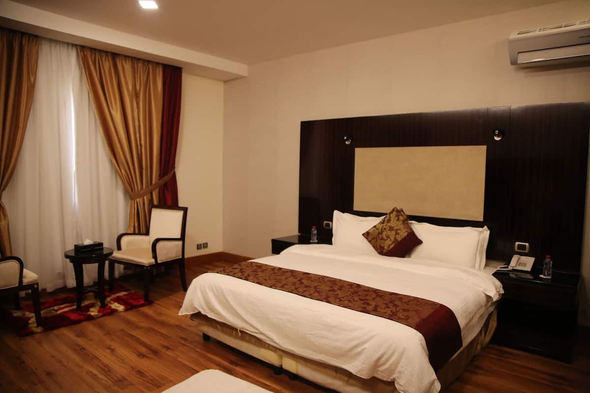 Une chambre d’hôtel avec un grand lit, une table de chevet avec un téléphone et une bouteille, une chaise et une petite table sur laquelle se trouve une boîte de mouchoirs.