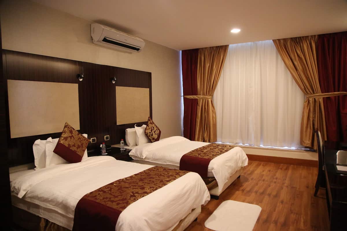 Une chambre d’hôtel avec deux lits, une grande fenêtre avec des rideaux, un plancher en bois et un climatiseur fixé au mur.