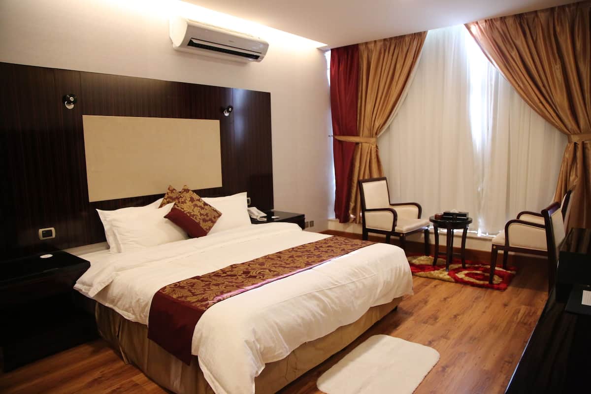Une chambre d’hôtel avec un grand lit, une table de chevet, une chaise, une petite table et un appareil de climatisation.