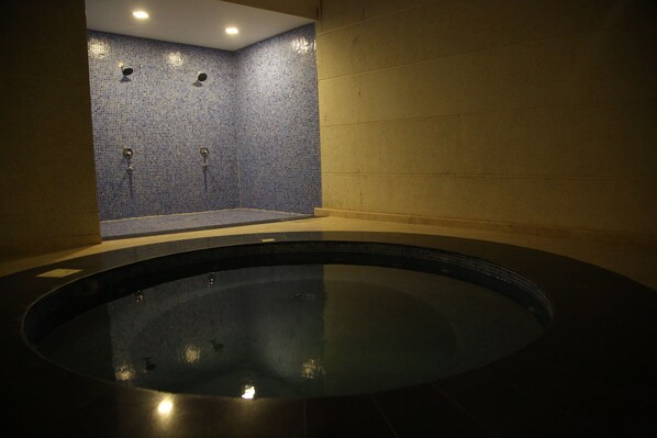 A spa area with a circular hot tub and a shower area with blue mosaic tiles. - Raoum Inn Hotel Apartments Corniche (Al Khafji)