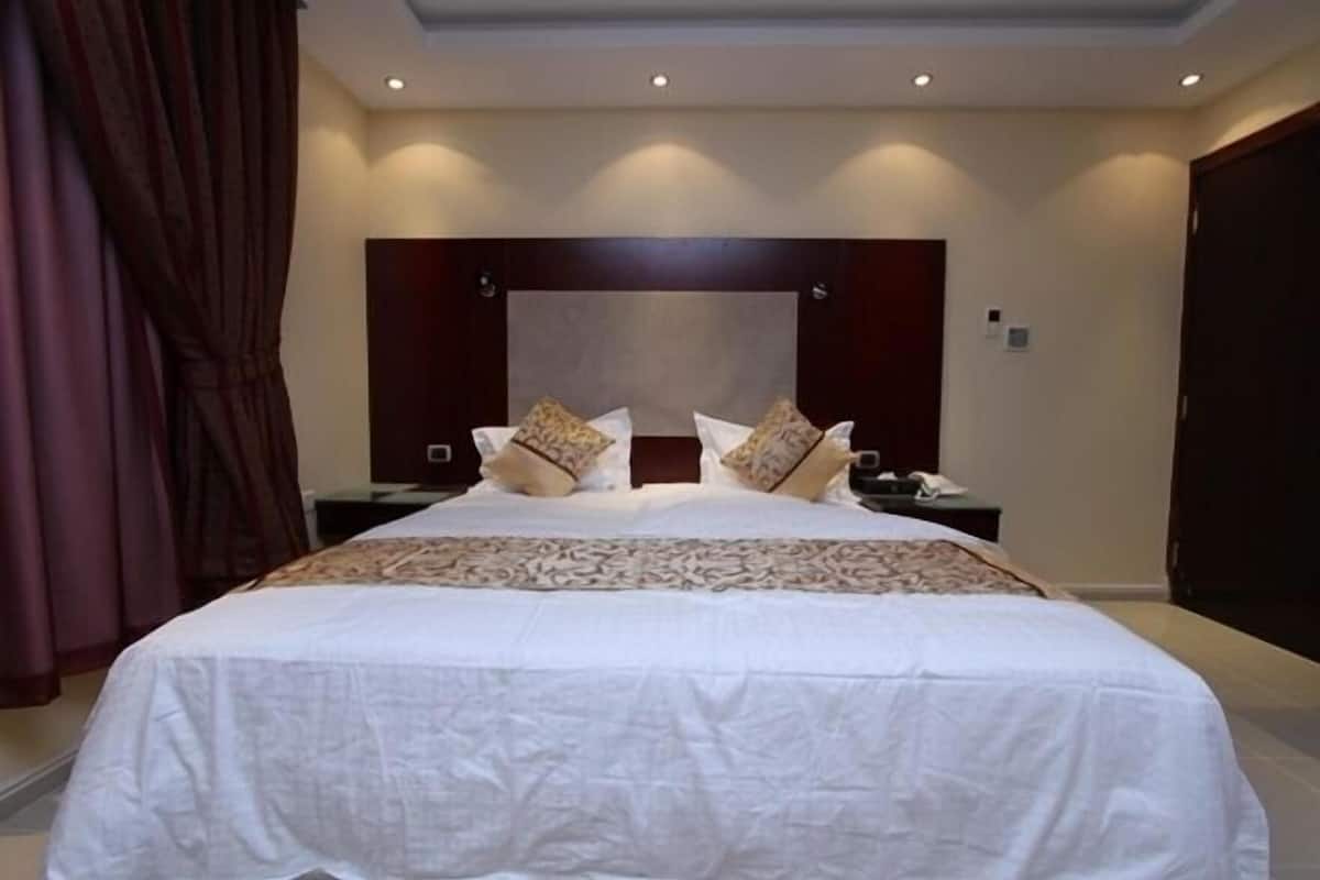 Una cama grande con una colcha estampada, dos mesitas de noche, un espejo grande y cortinas oscuras.