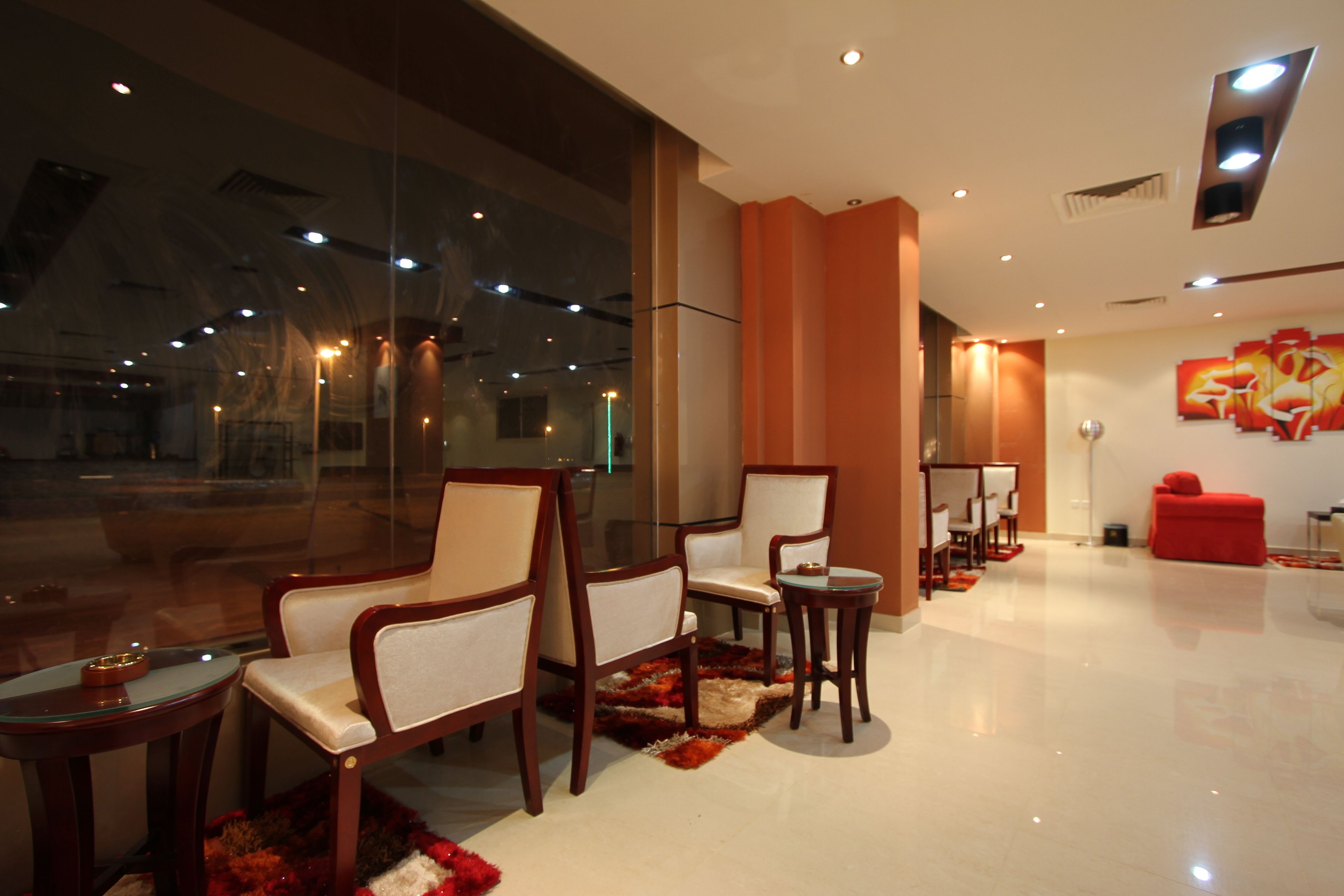 A modern hotel lobby with a glass wall, wooden chairs, a red sofa, and a small table.